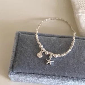 Detailansicht des silbernen Perlenarmbands mit Seestern und Muschel auf blauer Samtbox.