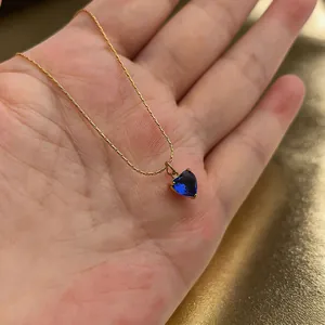 Detailopname van een blauwe hartvormige zirkoon hanger aan een gouden ketting