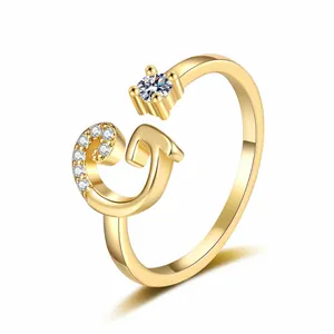 Detailed close-up of a gold-plated open ring with a sparkling crystal letter G and a zircon