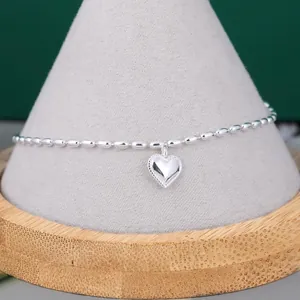 Dettaglio di un bracciale minimalista in argento con grani di riso e ciondolo a cuore.