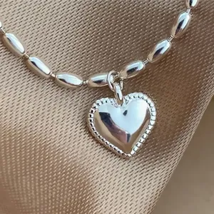 Dettaglio ravvicinato di un braccialetto in argento con perline di riso e cuore lucido.