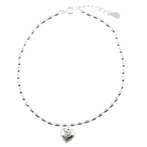 Dettaglio del bracciale in perle di riso argento con ciondolo a cuore su sfondo bianco.