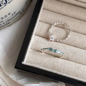 Nahaufnahme minimalistischer Perlenblumenring und gewellter blauer Emaille-Ring im Etui