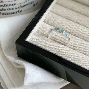 Makroansicht eines unregelmäßigen gewellten Silberrings mit hellblauem Emaille in einer Box.