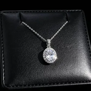 Detail view of oval cut moissanite pendant with halo diamonds on textured jewelry box.