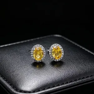 Macro detail of yellow oval moissanite stud earrings with diamond halo on black box.