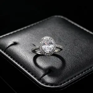 Macro detail shot of a classic oval-cut halo moissanite ring on a black jewelry box.