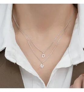 Close-up of layered S925 sterling silver necklaces with iced out D and M letter pendants.