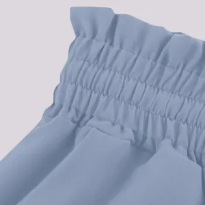 Close-up detail of dusty blue wide-leg pants with a ruffled high-waist elastic band.