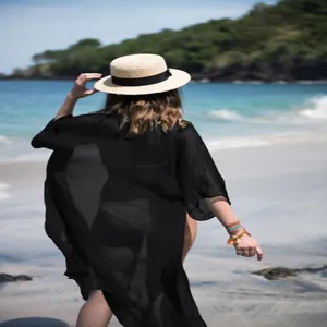 Back view of a long black chiffon beach cover-up worn over a bikini on a sunny shore