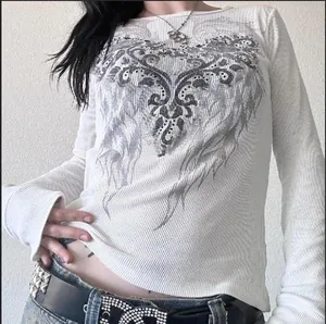 Detalle de un top blanco de manga larga ajustado con estampado de alas strass tipo retro.