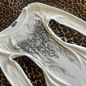 Detalle del estampado de alas de plumas y pedrería en camiseta de manga larga elástica