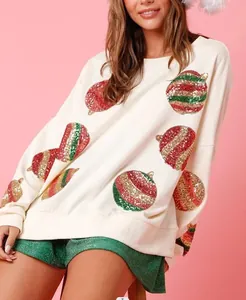 Détail d'un sweat-shirt crème avec broderie festive de boules de Noël en paillettes