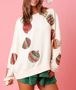 Sweatshirt de Noël blanc à ornements pailletés porté par un mannequin sur fond rose