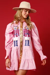 Close-up detail view of pink Christmas dress with sequined nutcracker and gold placket