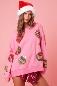 Femme en sweat rose festif orné de broderies colorées en paillettes de boules de Noël