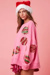 Détail du sweat de Noël rose avec des motifs de boules en paillettes colorées et style festif