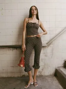 Full body shot of a model wearing a brown polka dot camisole and ruffled cropped pants.