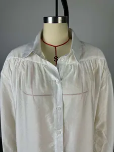Vue détaillée d'un chemisier blanc boutonné avec fronces aux épaules et col à revers.