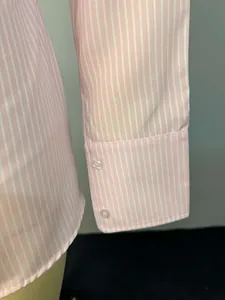 Primer plano detallado del puño de una camisa a rayas rosas y blancas con dos botones.