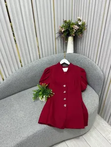 Elegante blazer rosso a maniche corte con bottoni dorati su un divano grigio di design