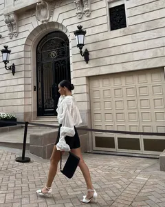 Femme marchant en chemisier blanc à manches lanterne et short noir devant l'architecture