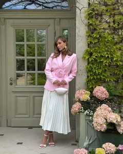 Model wearing pink blazer with 3D rose belt and white pleated skirt in garden setting