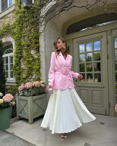 Elegant pink blazer with 3D flower detail and pleated white skirt in outdoor setting.