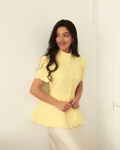 Vista dettagliata di un top giallo peplum con collo alto e design a bottoni a vita alta slim