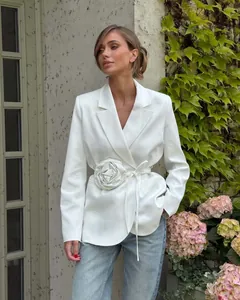 Detailed view of white blazer featuring a decorative 3D flower and adjustable waist tie.