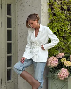 Model wearing a white blazer with a 3D flower and tied waist in an outdoor setting
