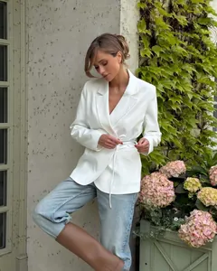 Model wearing an elegant white tie-waist blazer with blue jeans in a garden backdrop