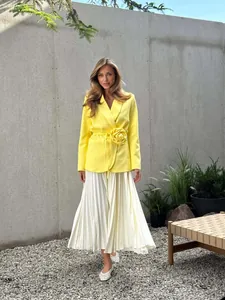 Elegant detail of a yellow blazer with a 3D flower waist belt and white pleated skirt