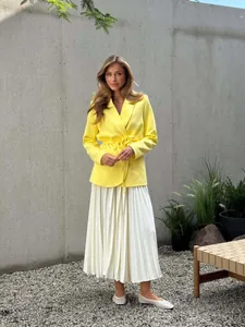 Detail view of a bright yellow belted blazer with 3D flower accent and pleated skirt