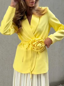 Close-up detail of stylish yellow blazer featuring a 3D flower and waist tie belt.