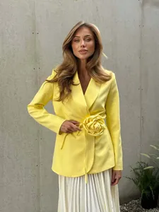 Detail view of yellow blazer featuring a large 3D floral accent and tie-waist