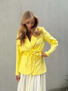 Detail view of a bright yellow blazer featuring a 3D flower and lace-up waist design