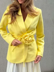 Detail view of yellow blazer featuring a large 3D flower decoration and waist tie