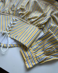 Detailed view of yellow and blue striped shirt with decorative lace-up waist design