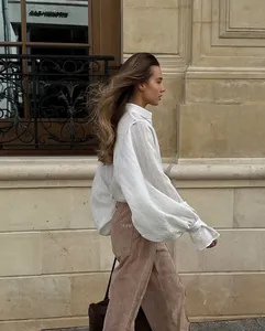 Full body side profile of a woman walking in a white oversized lantern sleeve blouse
