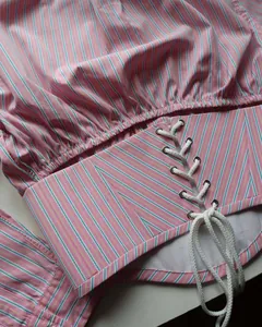 Close-up of pink striped shirt with elegant lace-up waist detail and metal eyelets.