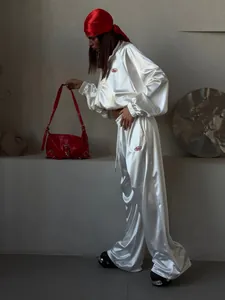 Model wearing a stylish white satin tracksuit with a loose hoodie and wide-leg pants
