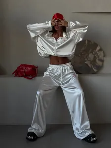 Detailed view of white satin zip-up tracksuit featuring glossy texture and red logo