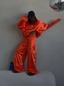 Full-body view of a stylish orange satin tracksuit with wide-leg pants and oversized sweatshirt