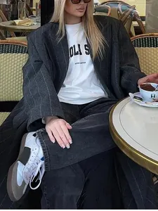 Detailansicht eines langen Nadelstreifenmantels mit Revers in einem Café-Ambiente.