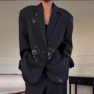 Detail eines schwarzen Oversize-Blazers mit Paillettenstickerei und feinen Nadelstreifen