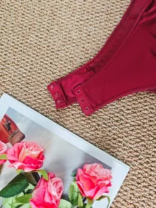 Close-up detail showing the secure snap button closure at the crotch of a dark red bodysuit