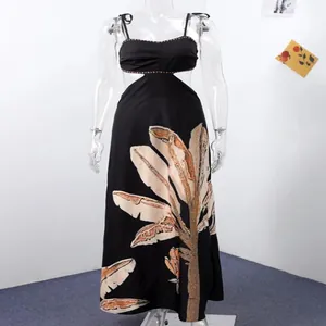 Detail of black maxi dress with waist cut-out and large tropical leaf print on skirt.