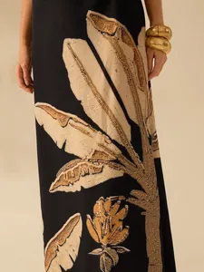 Close-up showing the intricate tropical leaf print texture on a black resort dress