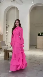 Élégante robe longue rose à volants étagés et col à nœud présentée dans une boutique.